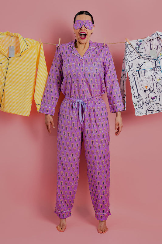 Person wearing a purple patterned outfit with colorful clothes on a line against a pink background